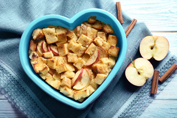 Delicious bread pudding with apples in heart shape bowl on napkin