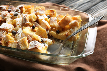 Bread pudding with raisins, walnuts and sugar powder in baking dish on table