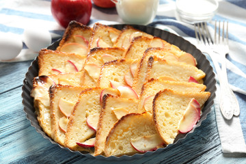 Tasty bread pudding with apples in baking dish on kitchen table