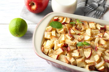 Tasty bread pudding with apples in baking dish on table