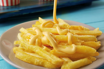 Pouring cheese sauce onto delicious fries, closeup
