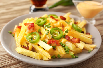 Tasty cheese fries with sliced pepper and sauce on wooden table