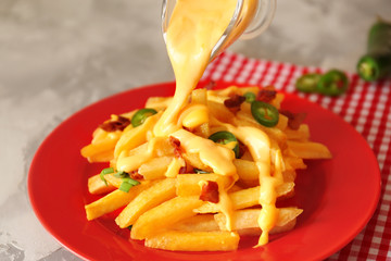 Pouring cheese sauce onto tasty fries on plate