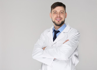 Young handsome pharmacist with crossed arms on grey background