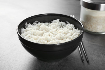 Bowl of rice and chopsticks on color background