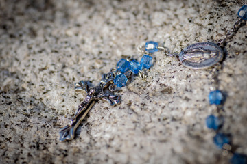 rosary and cross laying on rock in sunlight with vignette