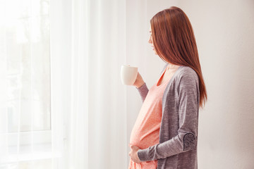 Beautiful pregnant woman standing near window at home