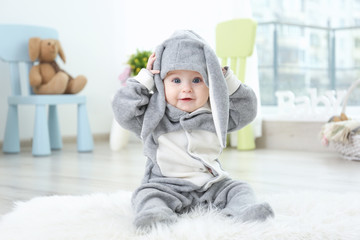 Cute little baby in bunny costume sitting on furry rug at home