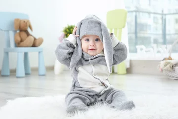 Fototapeten Cute little baby in bunny costume sitting on furry rug at home © Africa Studio