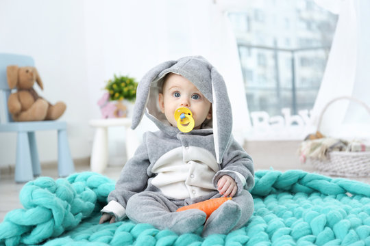 Cute little baby in bunny costume sitting on plaid at home
