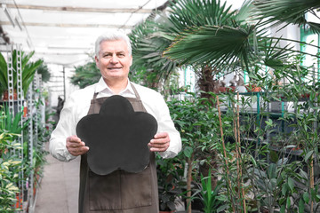 Male florist holding board with space for text in greenhouse