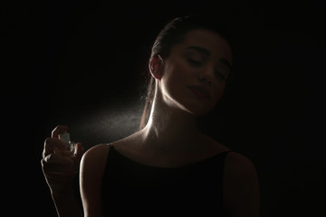 Beautiful young woman with bottle of perfume on dark background