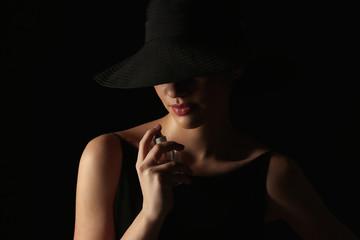 Beautiful young woman with bottle of perfume on dark background