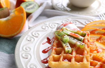 Tasty waffles with delicious fruits, ice-cream and syrup on white plate, close up
