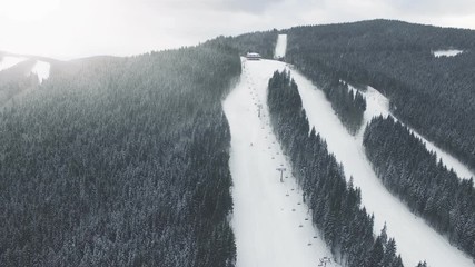 4K Aerial Drone View: Flight over winter mountains in the snowfall. Ski slopes with pine tree forest around. Majestic nature landscape. Holidays in Ski Resort Bukovel, Carpathian Mountains, Ukraine