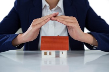 Businesswoman protecting house model with hands