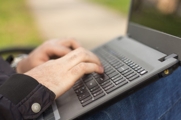 Young man in the park sitting on the bench with a laptop, close-up hands and laptop