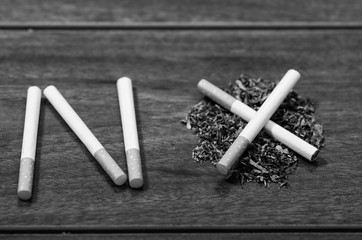 Cigarettes lying on wooden surface shaped into the word no, artistic anti smoking concept, black and white edition