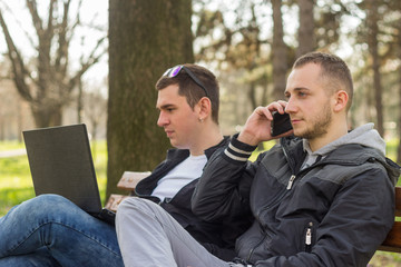 Two friendly male mature students outdoors in park sitting on bench.