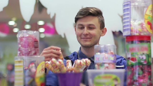 The young guy chooses a lollipop in the store