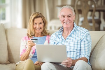 Smiling senior couple doing online shopping on laptop in living 