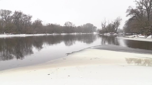 The river flows, snow-covered shore, shrubs, winter
