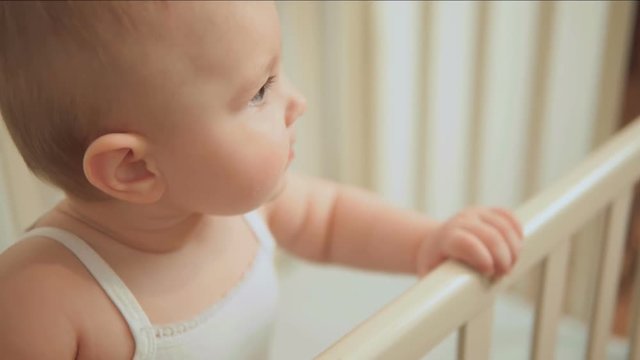 A cute little child is standing in a cot holding his hands over the sides