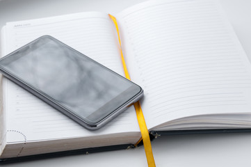 The cell phone is on open notebook with  yellow tab