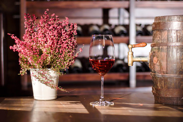 Composition of flower pot, wine glass and barrel placed on a wooden table. Shelves with wine...