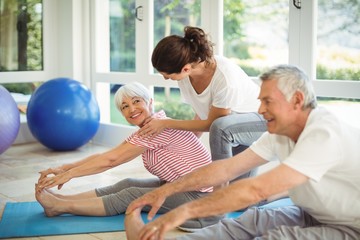 Female trainer assisting senior couple in performing exercise