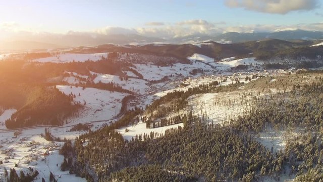 4K Aerial Drone View: Flight over Ski resort in winter, sunset time. Houses and hotels along the road. Pine tree forest around. Majestic nature landscape. Bukovel, Carpathian Mountains, Ukraine