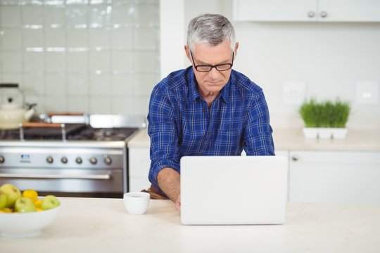 Senior Man Using Laptop In Kitchen