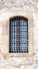 An ancient window with metal bars in an old fortification wall