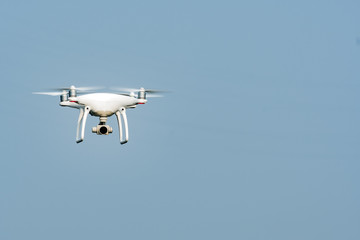 White drone, quadrocopter, with photo camera flying in the blue sky. Drone fly in the blue sky