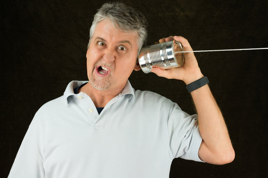 Funny face frustrated man on tin can phone representing old, crappy, outdated, antiquated technology, bad service, technical problems with telecommunication and phones, and bad computerized devices.