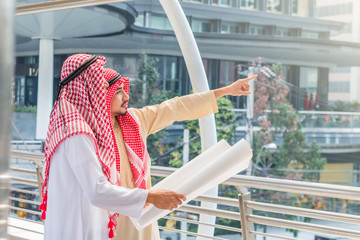 Portrait of arabian engineer talking about construction job and verify the blueprint with commitment to success in downtown with building background