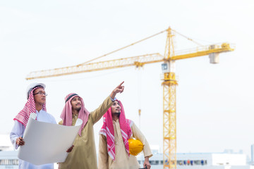 Portrait of arabian engineer talking about saudi job and verify the blueprint with commitment to success at construction site with crane background