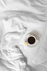 A mug of black coffee is standing on a white bed