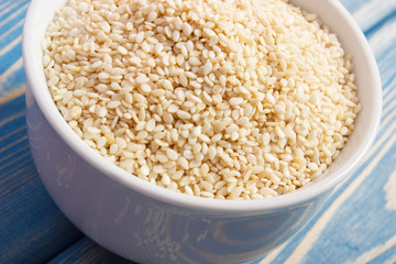 Heap of sesame seeds in white bowl on wooden boards