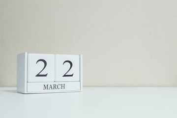 Closeup white wooden calendar with black 22 march word on blurred white wood desk and cream color wallpaper in room textured background with copy space , selective focus at the calendar