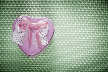 Metal pink heart-shaped gift box with ribbon on green background