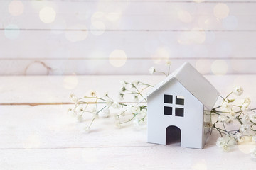 Miniature white toy house with flowers on a white wooden background.