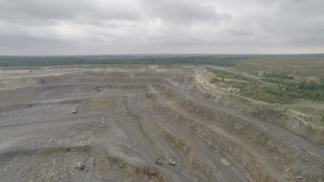 Video footage taken from a height over a giant quarry. Flight over a deep crater. The production of useful types of heavy vehicles. Excavations in the bowels of the earth. Storm clouds and giant bat.