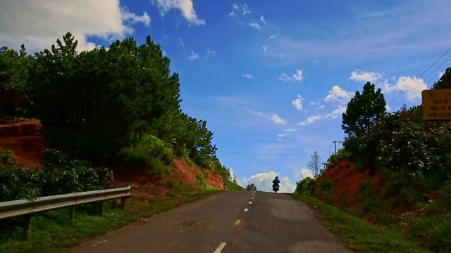 Camera Follows Scooter along Country Road among Hilly Landscape