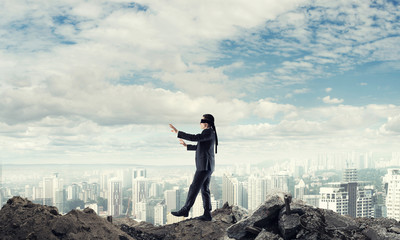 Young businessman in blindfold walking carefully and cityscape at background