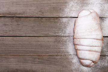 one croissant sprinkled with powdered sugar on old wooden background with copy space for your text. Top view