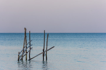 A frame made from old wooden posts stands in a calm sea at golden hour.