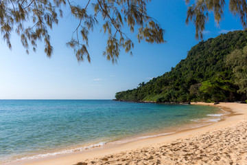 White sandy beach bay with forested headland in the distance on a tropical island.