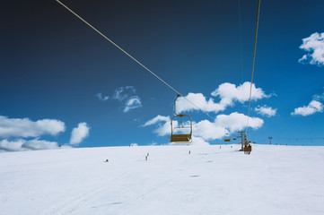 Ski lift with seats going over the mountain and paths from skies and snowboards with beautiful blue sky and clouds on background. Karpatians, Ukraine