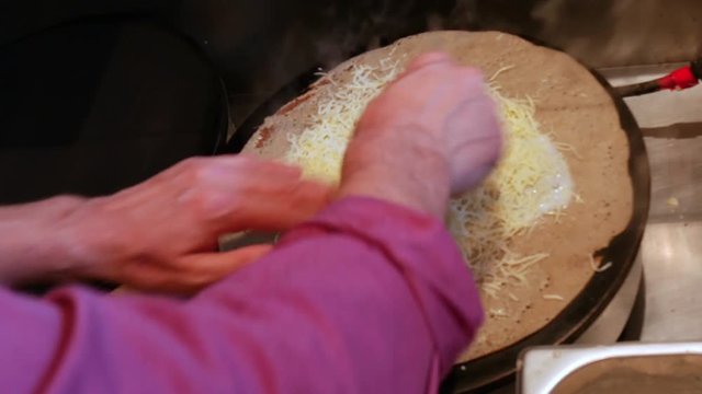 4K close up of a man adding cheese to a crepe, or buckwheat pancake, in his crêperie restaurant, in Brittany. Galettes complètes, creperie, Rennes, Bretagne, France.